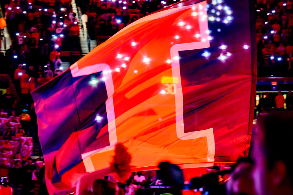 large Block I flag backlit in a dark State Farm Center during Illinois basketball game