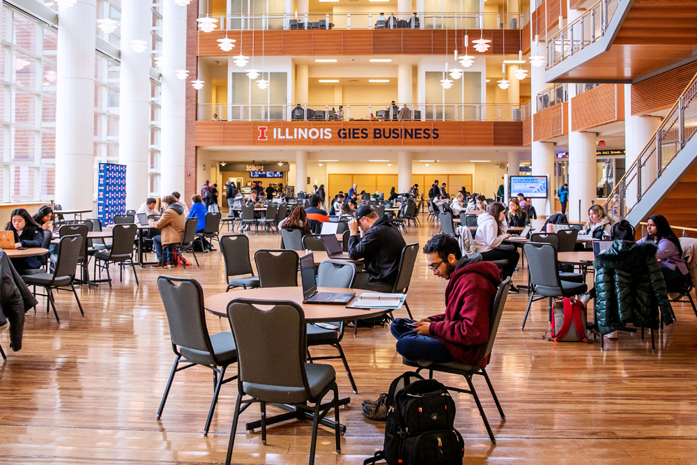 students sit and work between classes in the atrium of the Gies College of Business Business Instructional Facility