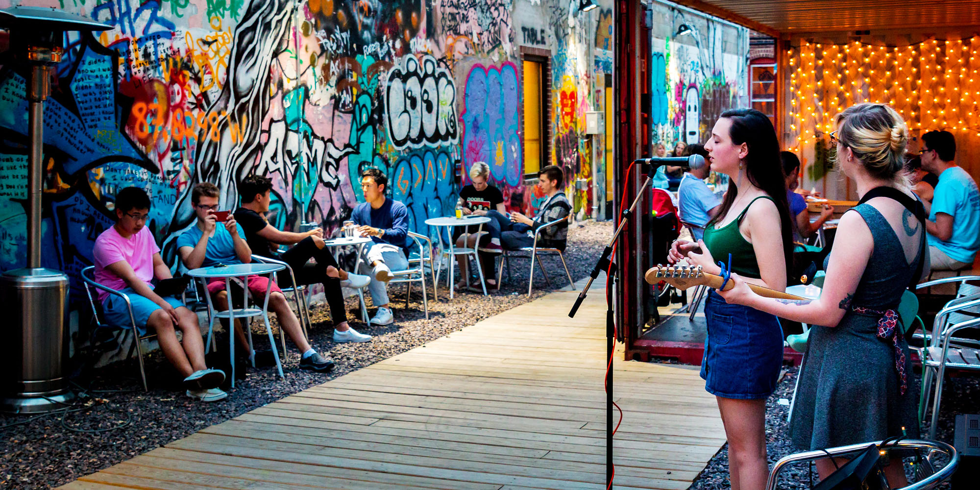 students listen to others perform at a venue in downtown Urbana surrounded by murals, graffiti, and lights