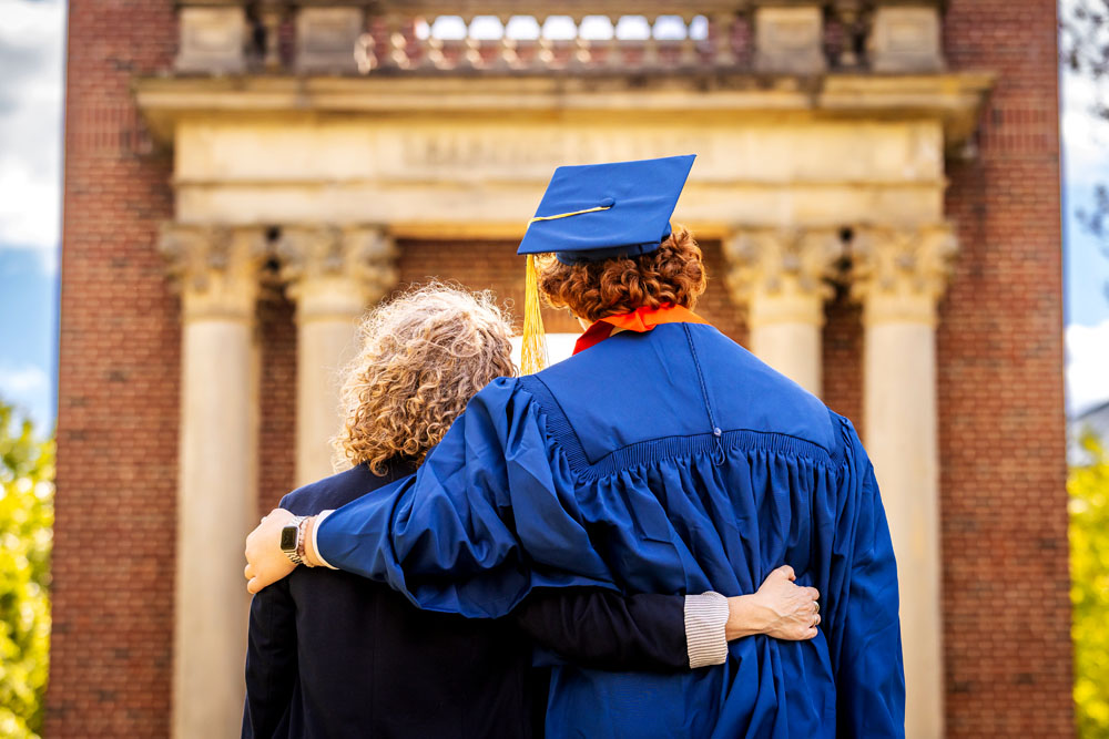 mother and graduating son hug and face the Hallene Gateway, popular photo op and landmark that welcomes most visitors to the east side of campus
