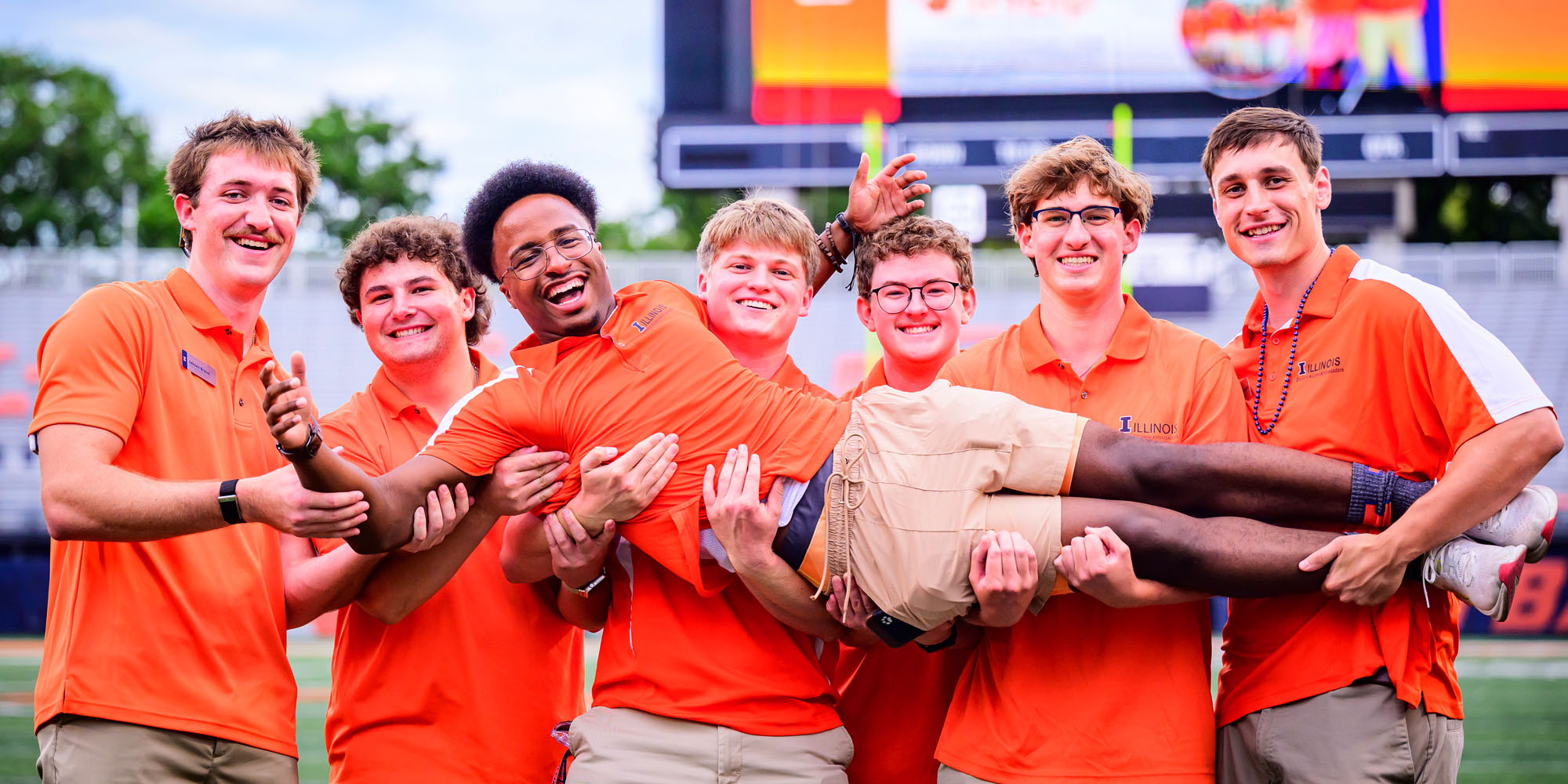 group of friends dressed in orange lift and hold up one of their own at Sights and Sounds welcome event for new, incoming students