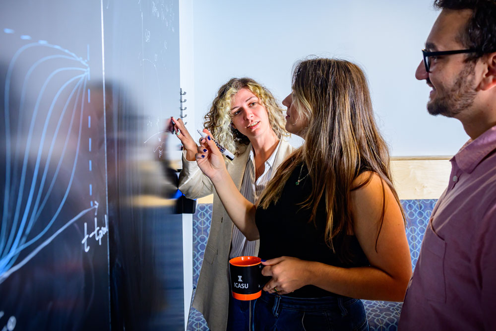 Theoretical nuclear physicist Jaki Noronha-Hostler works with two research students at a whiteboard in Loomis Laboratory