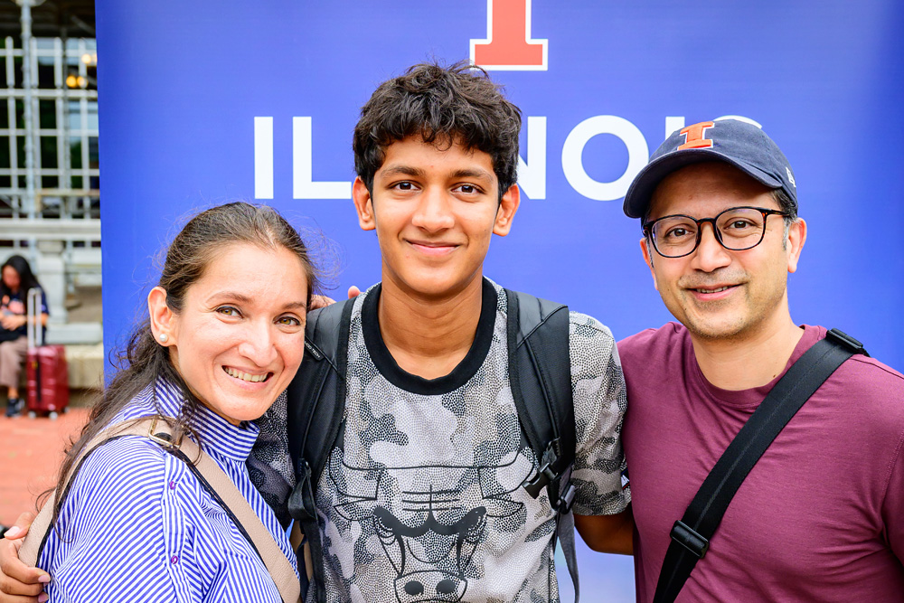 parents and son pose in front of Illinois backdrop at family send-off event outside the Illini Union