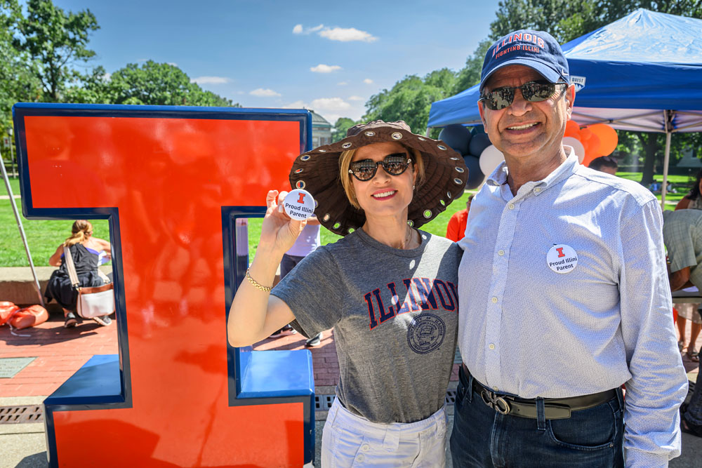 proud Illinois parents pose with buttons and large Block I on the Quad during new student welcome event