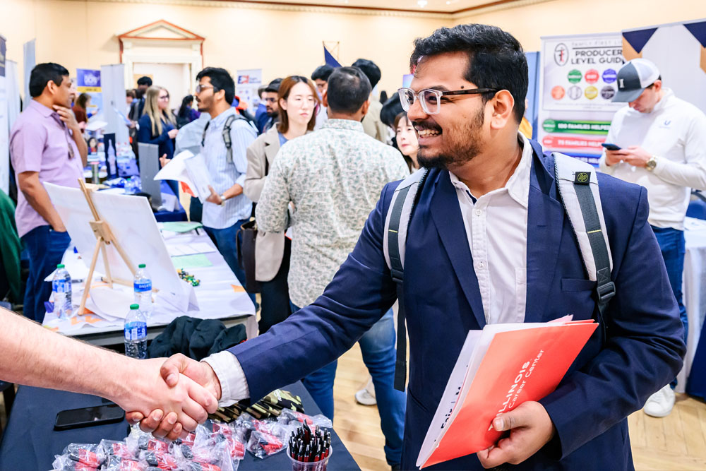 well-dressed student shakes hands and introduces themselves to recruiter at Illinois career fair