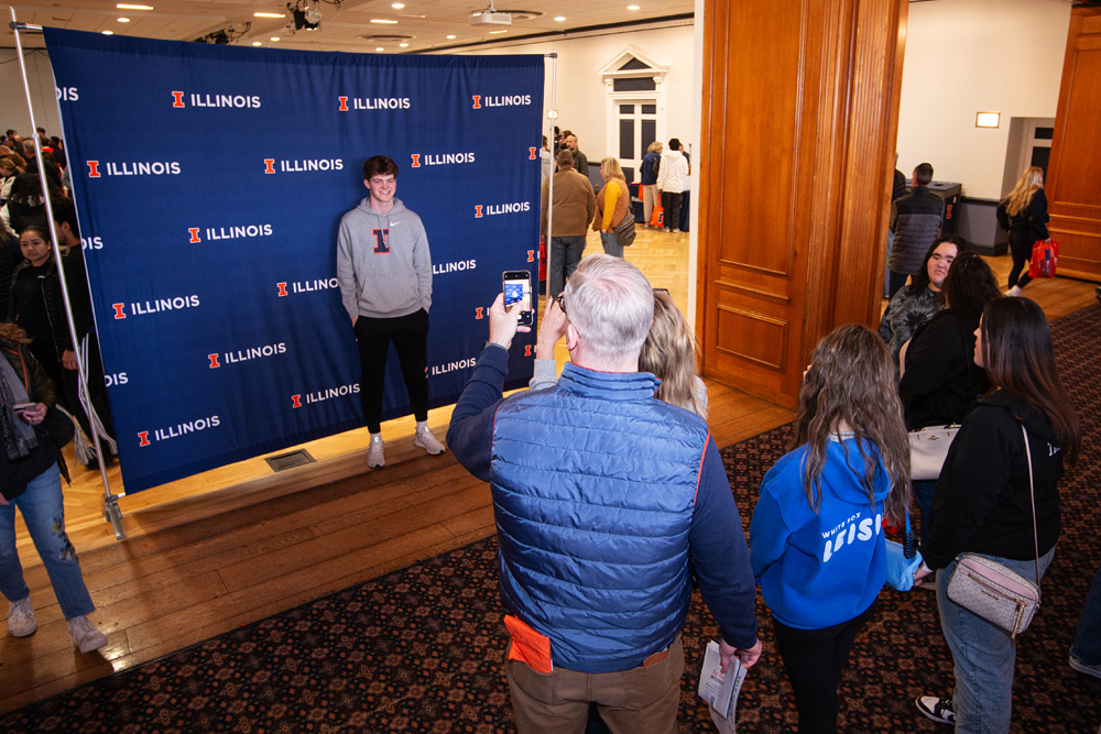 family takes a photo op with blue backdrop branded with Illinois wordmark at IlliniFest