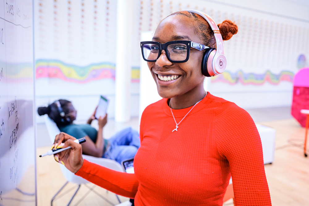 smiling student wearing headphones and writing on a white board