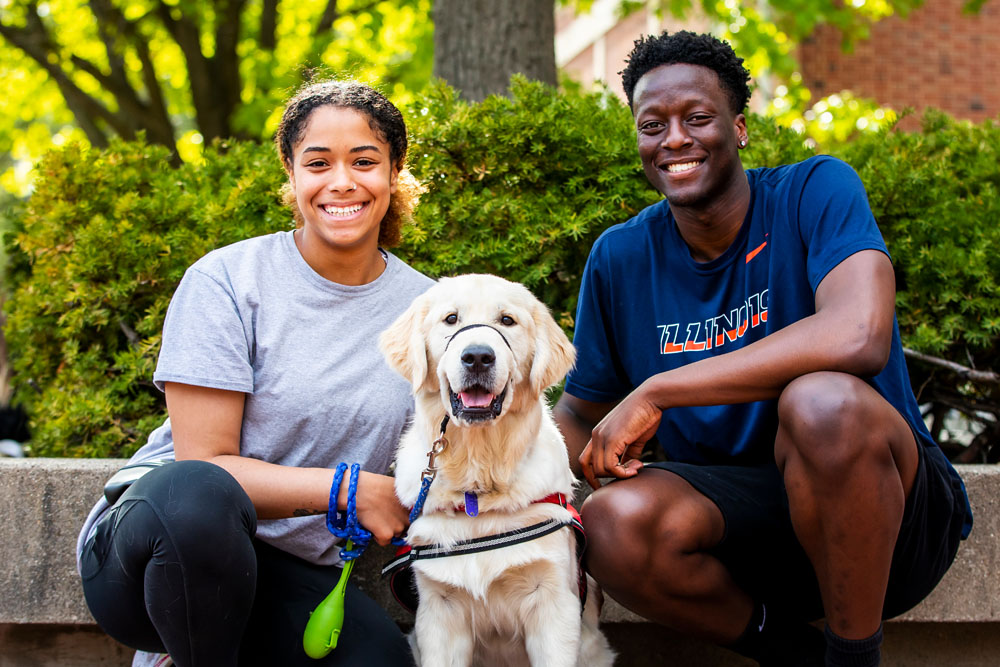 two Illinois students pose with service animal outside the Illini Union