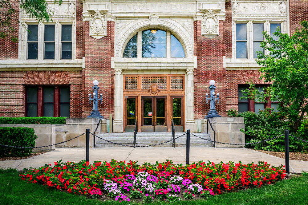 Lincoln Hall's main entrance off the Quad with red and pink flowers